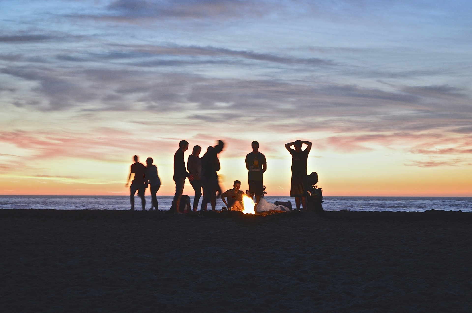 People around a beach bonfire at dusk, the sea behind them