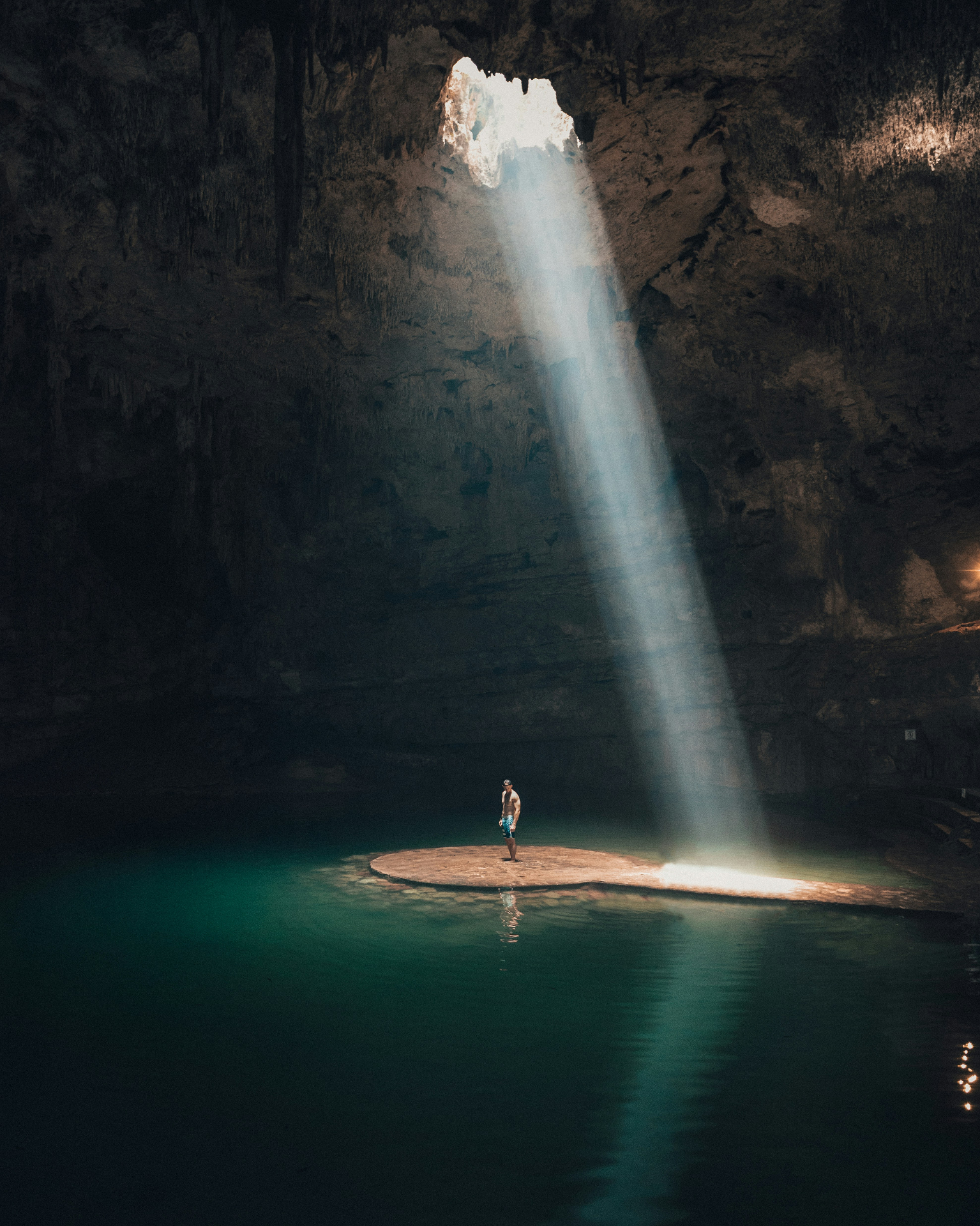 A person under a shaft of light in a turquoise cenote