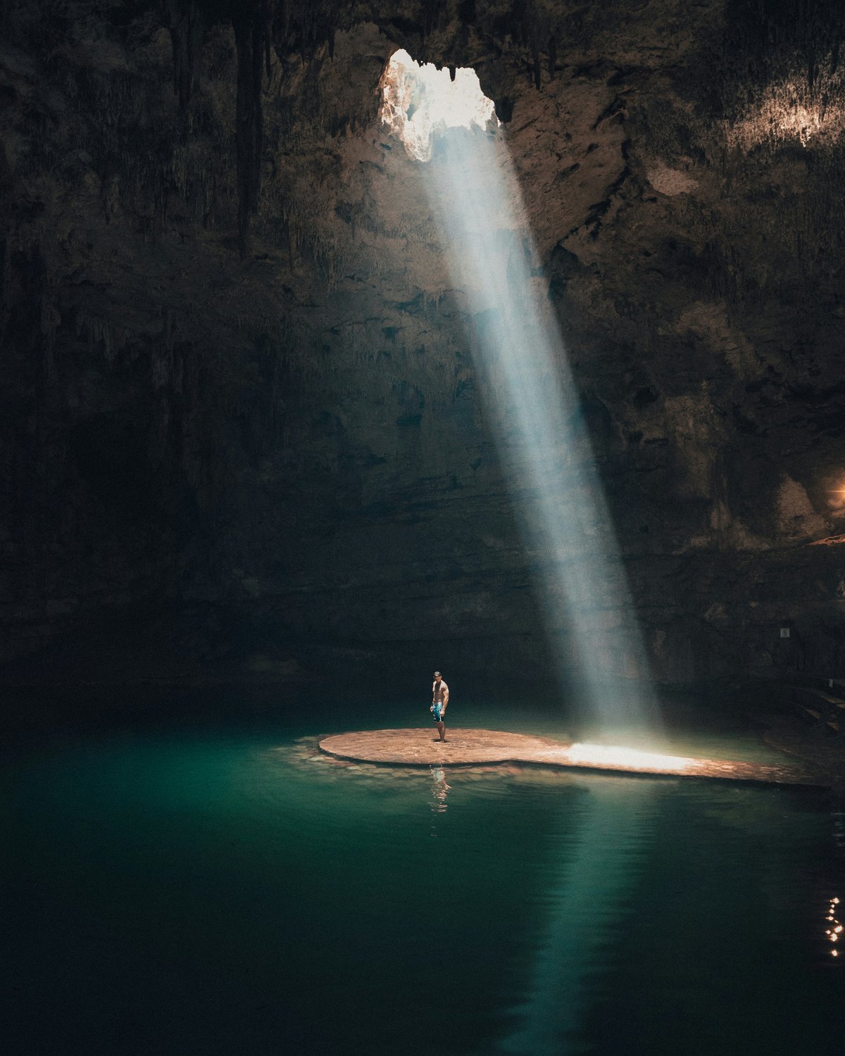 Persona bajo un haz de luz en un cenote de aguas turquesas